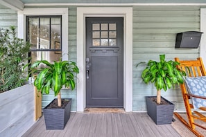 A porch with two potted plants, a dark door, and a wooden chair. - Parkside 1922 - Steps to Boone Park & Avondale Shops (Jacksonville)