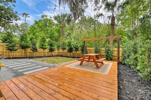 Eine Holzterrasse mit Picknicktisch und Schaukel, umgeben von einem Holzzaun und üppigem Grün.