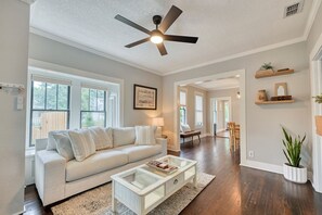 A living room with a ceiling fan, a sofa, a glass coffee table, and a dining area in the background. - Parkside 1922 - Steps to Boone Park & Avondale Shops (Jacksonville)