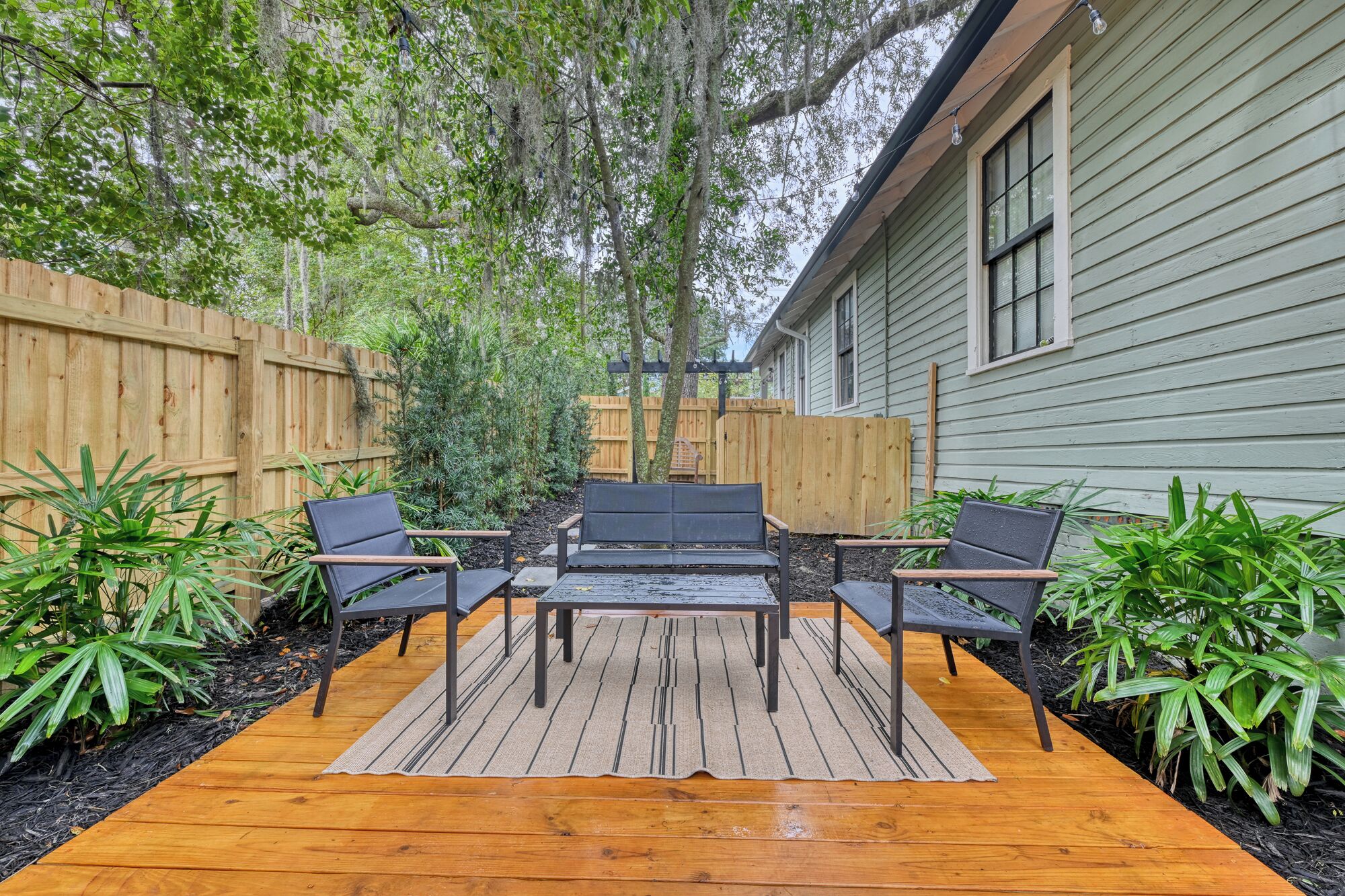 Un patio al aire libre con terraza de madera, una mesa de metal y cuatro sillas.