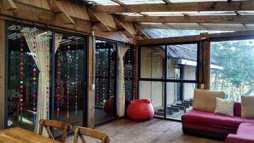 A wooden interior with a glass door leading outside, a red bean bag chair, and a wooden table with chairs.