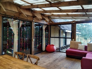 Een houten interieur met een glazen deur naar buiten, een rode hangstoel en een houten tafel met stoelen.