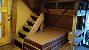 A wooden bunk bed with a mattress, a wooden staircase, and a door.