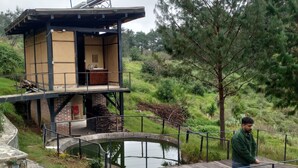 A modern outdoor structure with a wooden deck, a small pond, and a metal fence.