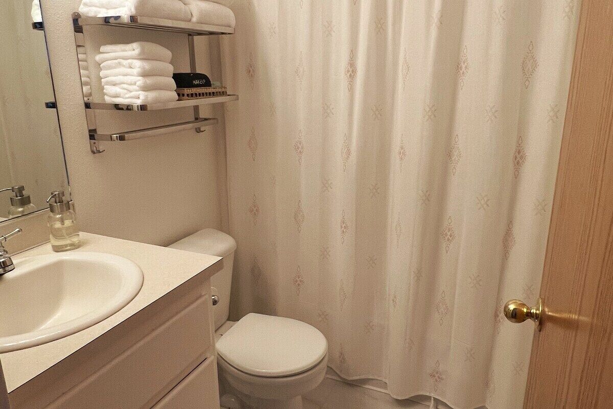 Kylpyhuone, jossa on wc, pesuallas, peili ja hylly, jossa on siististi taiteltuja pyyhkeitä.