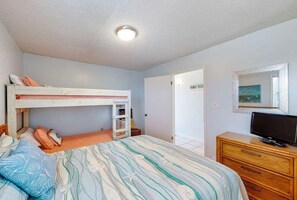 Ein Schlafzimmer mit Etagenbett, einem Schminktisch, einem Fernseher und einer Tür zu einem anderen Raum.
