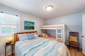 A bedroom with a bunk bed, a single bed, a bedside table, a chair, and a painting on the wall. - Buena Vista 405 | Beachfront | Beach Side Pool | Low-Density | My Beach Getaways (Gulf Shores)