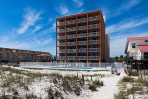 Ein mehrstöckiges Hotel mit Pool, gelegen an einem Sandstrand, im Hintergrund sind weitere Gebäude zu sehen.