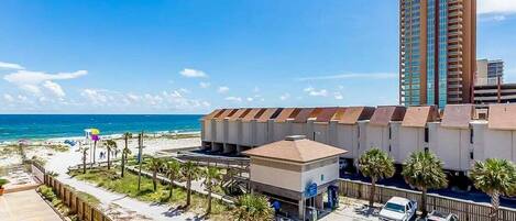 Un hôtel situé en bord de mer, doté d’un parking, d’une plage et d’un grand immeuble en arrière-plan.