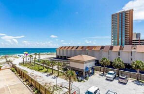 Ein Hotel direkt am Strand mit Parkplatz, Strand und einem hohen Gebäude im Hintergrund.