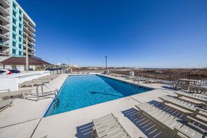 Ein rechteckiger Pool mit klarem, blauem Wasser, umgeben von Liegestühlen und einem Gebäude mit Balkonen.