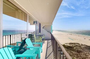Een balkon met stoelen en een tafel, met uitzicht op een strand.