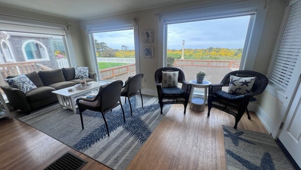Ein geräumiger Wohnbereich mit Sofa, Sesseln, einem Couchtisch und Blick auf einen umzäunten Garten durch große Fenster.
