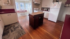 Eine Küche mit Holzboden, weißen Schränken, einem Kühlschrank und einem Essbereich mit Tisch und Stühlen.