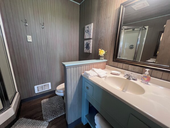 Un baño con pared de paneles de madera, un lavamanos blanco con espejo, un perchero y un pequeño florero con flores.