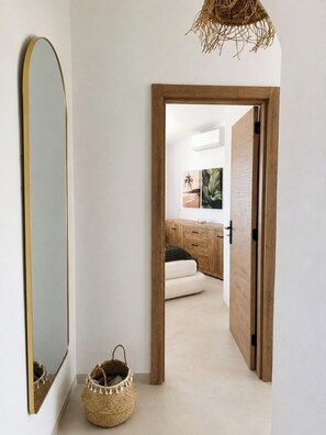 A hallway leading to a room with a wooden door, a mirror, and a woven basket. - Bright 2-BR Apt with Spacious Terrace and Sea Views (Carvoeiro)
