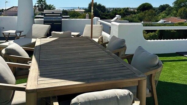 Eine Terrasse im Freien mit Tisch und Stühlen, einem großen Sonnenschirm und Blick auf die Landschaft.