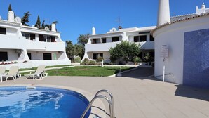 Ein Swimmingpool mit Liegestühlen, einer gefliesten Terrasse und weißen Gebäuden mit mehreren Balkonen.