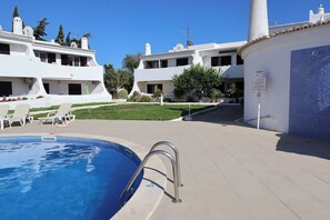 A swimming pool with lounge chairs, a tiled deck, and white buildings with multiple balconies. - Bright 2-BR Apt with Spacious Terrace and Sea Views (Carvoeiro)