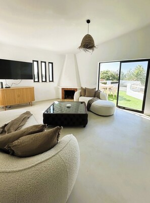 A modern living room with a flat-screen TV, a fireplace, a glass coffee table, and a large window offering a view of the outdoors. - Bright 2-BR Apt with Spacious Terrace and Sea Views (Carvoeiro)
