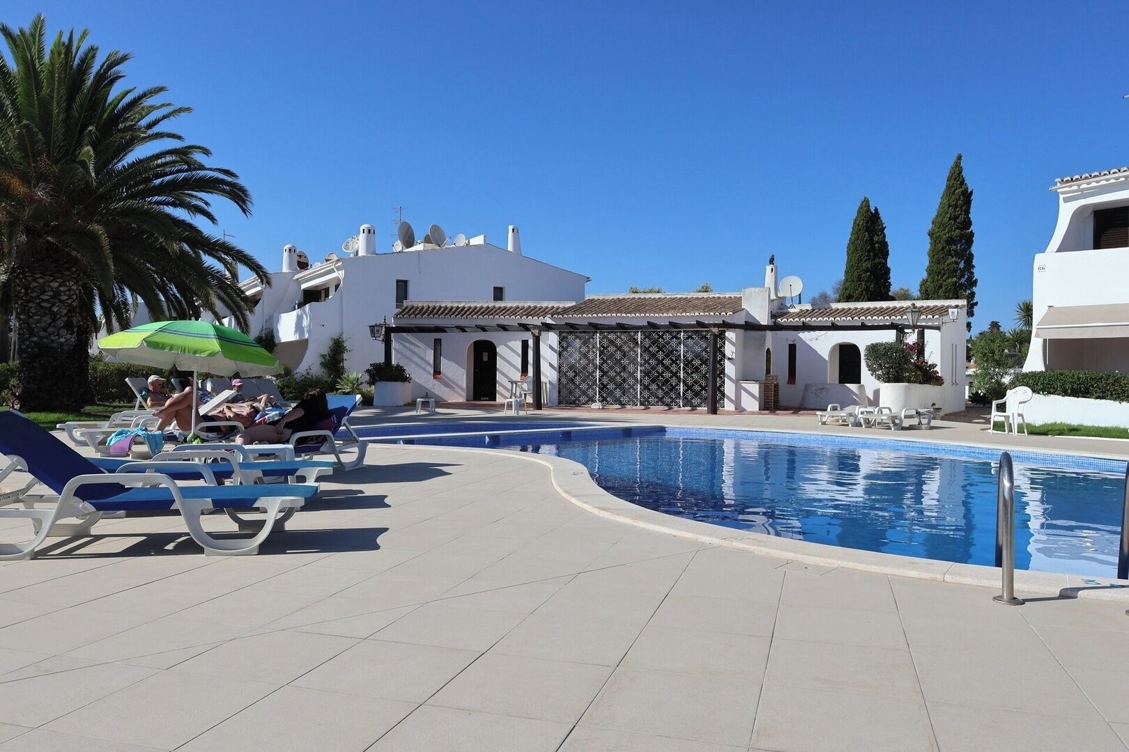 A pool area with lounge chairs and a building with a tiled roof.