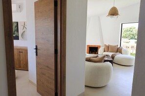 A modern interior with a wooden door, a white sofa, and a hanging light fixture. - Bright 2-BR Apt with Spacious Terrace and Sea Views (Carvoeiro)