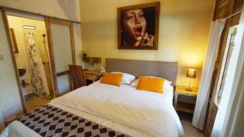 Habitación de hotel con una cama grande, dos mesitas de noche, un sillón, un cuadro en la pared y un baño visible a través de una puerta abierta.