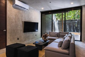 A modern living room with a large flat-screen TV mounted on the wall, a sectional sofa, and two black ottomans. - Casa Naya - 2 Pools, Near Beach, VIP Concierge (Tulum)