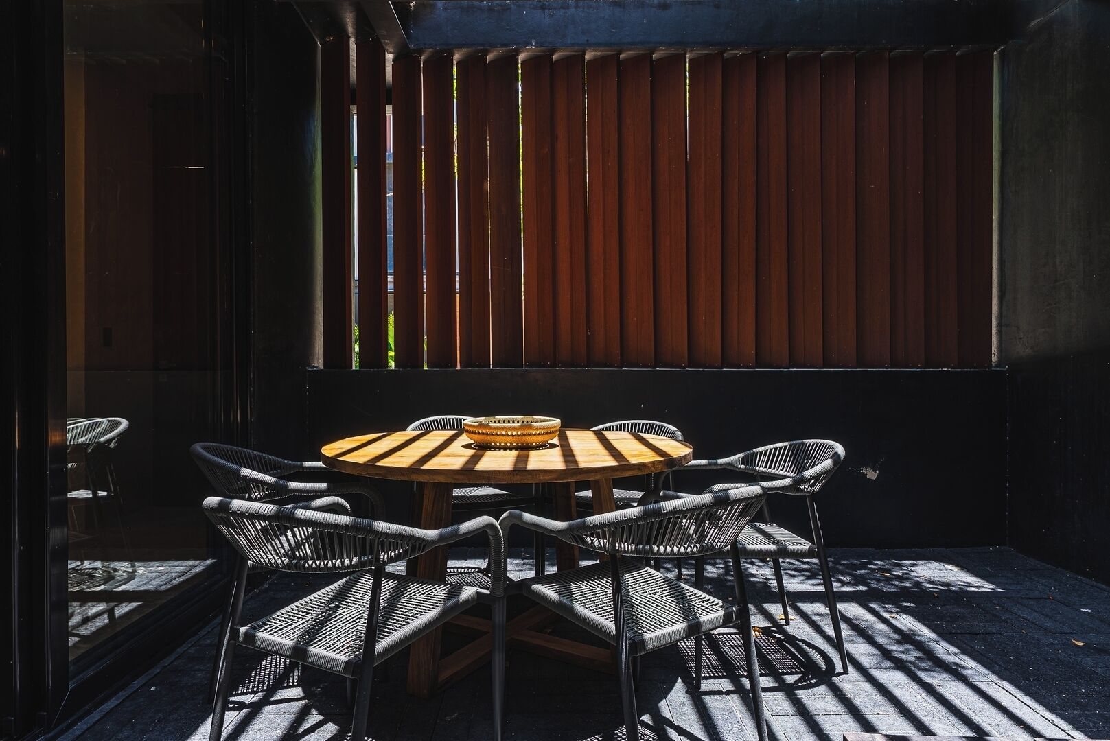 Una mesa redonda de madera con una cesta tejida en el centro, rodeada de cuatro sillas de mimbre.