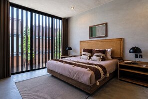 A modern bedroom with a large bed, a wooden headboard, a nightstand, a bedside lamp, and a view through floor-to-ceiling windows. - Casa Naya - 2 Pools, Near Beach, VIP Concierge (Tulum)