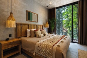 A bedroom with a large bed, wooden headboard, two bedside tables, a hanging lamp, a framed picture, and a view of greenery through a window. - Casa Naya - 2 Pools, Near Beach, VIP Concierge (Tulum)