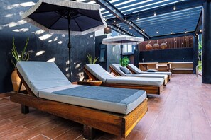 A sunlit outdoor lounge area with wooden loungers, a concrete table, and a pergola structure. - Casa Naya - 2 Pools, Near Beach, VIP Concierge (Tulum)