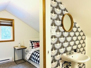 Ein Schlafzimmer mit Bett, Nachttisch und Fenster. Das Zimmer verfügt über eine Schräge und eine Heizung.