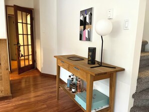 Een houten bureau met een lamp, een blikje en een doos in een kamer met een houten vloer en een deur op de achtergrond.