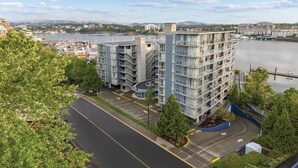 A multi-story hotel with a curved driveway, located near a body of water with a bridge in the background. - Peak July Escape! Spacious 2BR Suite in the Heart of Victoria (Victoria)