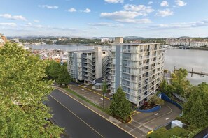 A multi-story hotel with a curved driveway, located near a body of water with a bridge in the background. - Peak July Escape! Spacious 2BR Suite in the Heart of Victoria (Victoria)