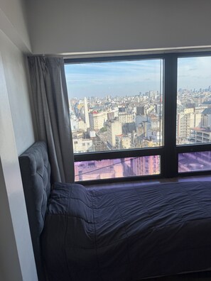 Une chambre avec un lit et une grande fenêtre donnant sur un paysage urbain.