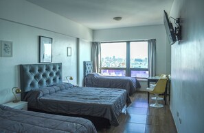 Quarto de hotel com duas camas, uma escrivaninha e vista para a cidade.