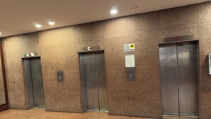 Tres portes d'ascensor en un passadís amb paret amb relleu i terra amb moqueta.
