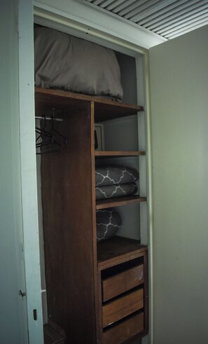 A wooden closet with shelves and drawers, a hanging rod, and a ceiling vent.