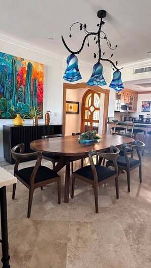 Uma sala de jantar com uma mesa redonda de madeira, seis cadeiras e um lustre moderno.