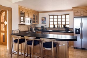 A kitchen with a central island, bar stools, a refrigerator, and a window with a view. - Newly Remodeled! No Lock Off-2BR at Estancia! Lavish furnishings, amenities and view! (Cabo San Lucas)