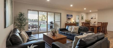 A modern living room with a leather sofa, a coffee table, and a dining area with wooden chairs and a table.