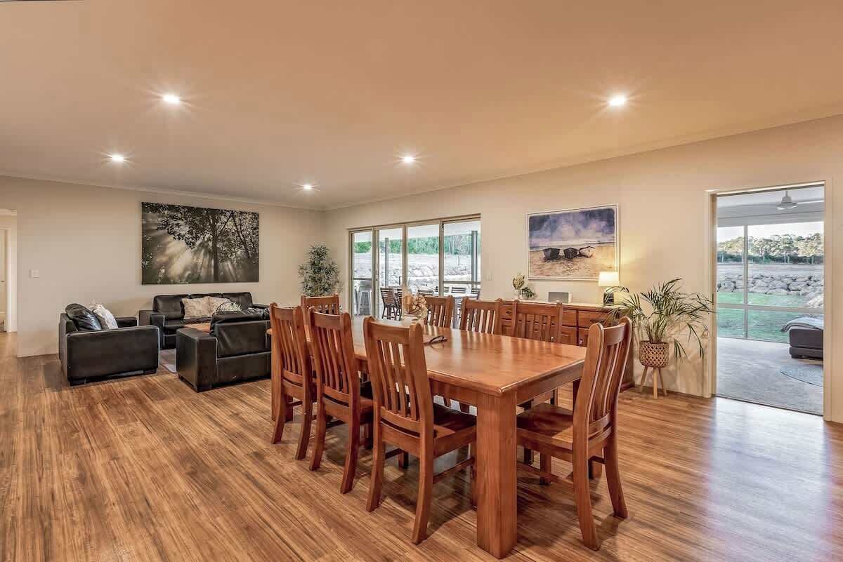 A spacious living area with a wooden dining table, comfortable seating, and large windows offering views of the outdoors.