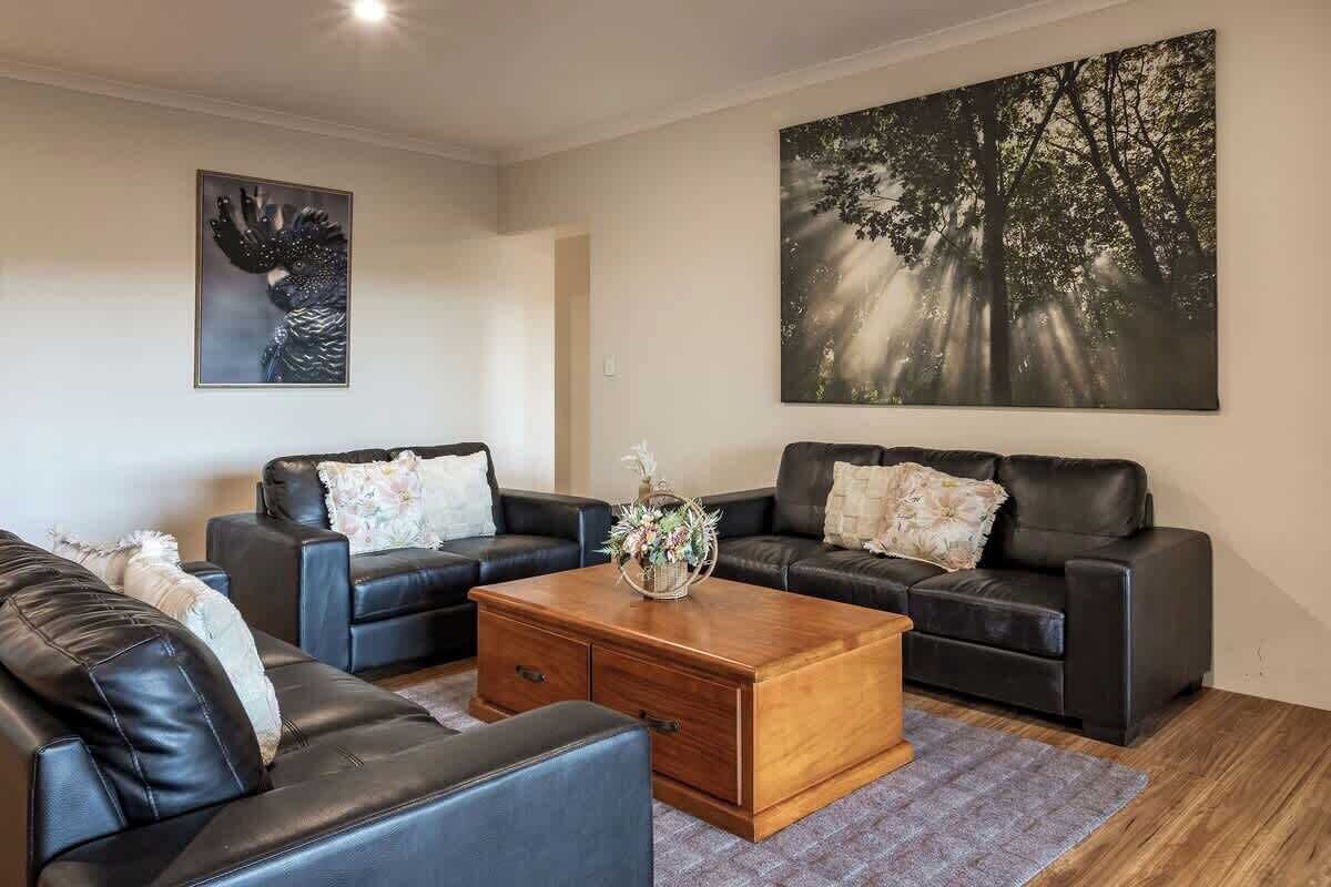 A living room with two black leather sofas, a wooden coffee table, and a large forest-themed painting on the wall.