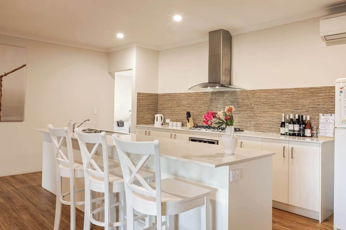 A modern kitchen with white cabinetry, a central island, and a stainless steel range hood.