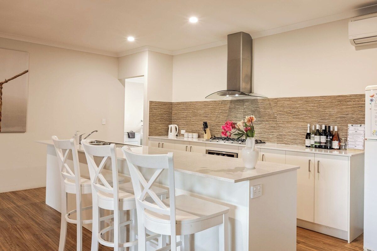 A modern kitchen with a central island, white cabinetry, and a stainless steel range hood.