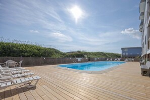 Ett trädäck med en pool, solstolar och utsikt över havet.