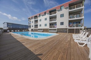 A multi-story hotel with a pool area, wooden deck, and outdoor seating. - 5621 - Dolphin Cove Oceanfront 2BR condo with pool, deck access, and direct beach views. (Nags Head)