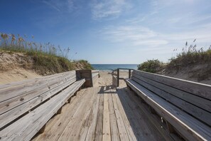A wooden boardwalk leading to a beach with benches and a small structure. - 5621 - Dolphin Cove Oceanfront 2BR condo with pool, deck access, and direct beach views. (Nags Head)